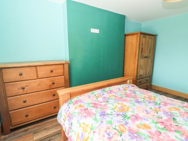 A bedroom with a wooden bed with floral bedding a wooden dresser and a wooden wardrobe at Lack Cottage in Annascaul near Camp County Kerry