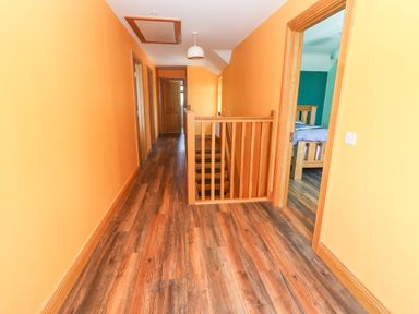 A hallway with wood flooring and orange walls with doors leading to rooms at Lack Cottage in Annascaul near Camp County Kerry