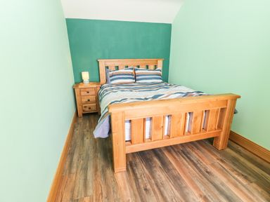A bedroom with a wooden bed frame and nightstand with a lamp at Lack Cottage in Annascaul near Camp County Kerry