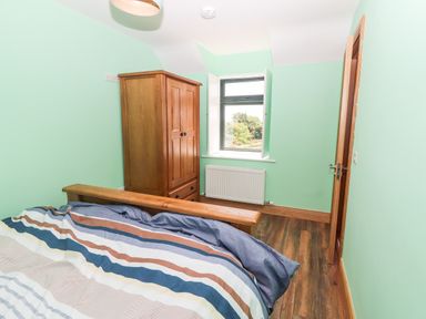 A bedroom with a bed a wooden wardrobe a window and a partially open door at Lack Cottage Annascaul near Camp County Kerry
