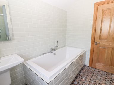 A bathroom with a bathtub sink wooden door and patterned floor tiles at Lack Cottage in Annascaul near Camp County Kerry