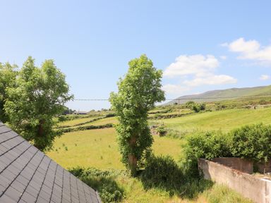 A countryside landscape with trees fields and hills with a roof visible in the foreground at Lack Cottage in Annascaul near Camp County Kerry