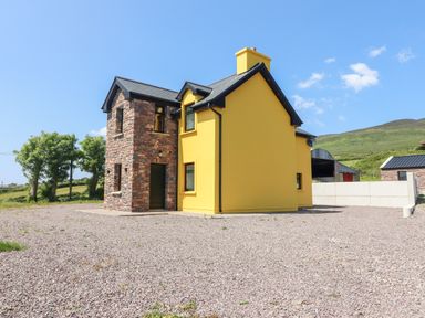 A yellow house with a stone chimney and a gravel yard at Lack Cottage in Annascaul near Camp County Kerry