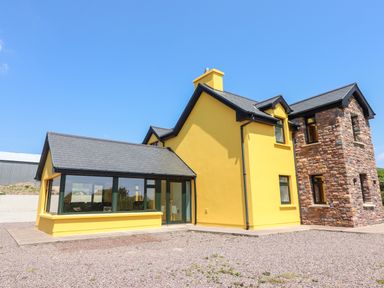 A yellow house with large windows and a stone extension at Lack Cottage Annascaul near Camp County Kerry