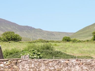 A stone wall with green fields and hills in the background at Lack Cottage in Annascaul near Camp County Kerry