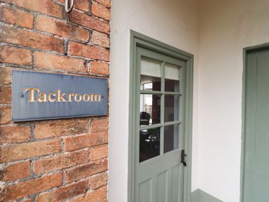 A green door with glass panes next to a brick wall with a Tackroom sign at The Tack Room in Lydney