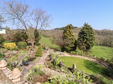 A garden with a stone pathway lawn trees and shrubs overlooking a field at The Tack Room in Lydney