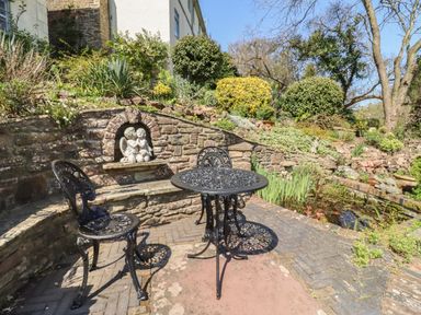An outdoor patio with a metal table and chairs stone wall with a cherub sculpture and garden pond at The Tack Room in Lydney