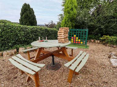 An outdoor seating area with a round wooden table and benches with games including large block tower and connect four at The Tack Room in Lydney