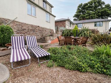 An outdoor garden area with two striped lounge chairs and a wooden table with chairs surrounded by plants at The Tack Room in Lydney