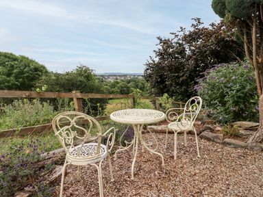 A garden area with two metal chairs and a round table on wood chip ground at The Tack Room in Lydney