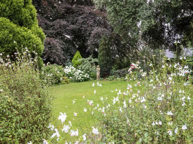 A garden with green grass white flowers bushes trees and a small statue at The Tack Room in Lydney