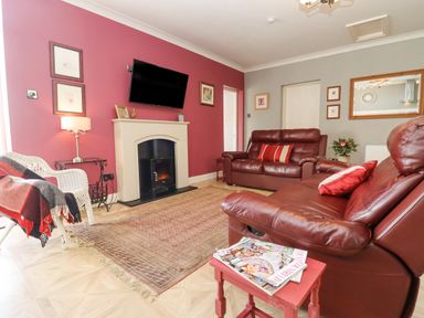 A living room with red walls two leather sofas and a television above a fireplace at The Tack Room in Lydney