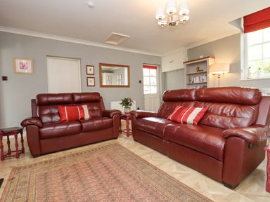A living room with two red leather sofas a patterned rug a bookshelf and a window at The Tack Room in Lydney