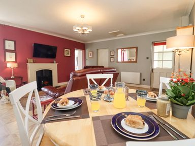 A dining table set with plates of pastries and glasses of orange juice in a living room with a red accent wall and a fireplace at The Tack Room in Lydney