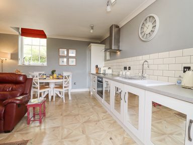 A kitchen with white cabinets dining table set with chairs and a red sofa at The Tack Room in Lydney