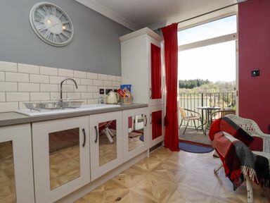 A kitchen with white cabinets and mirrored doors red curtains and a small outdoor seating area at The Tack Room in Lydney