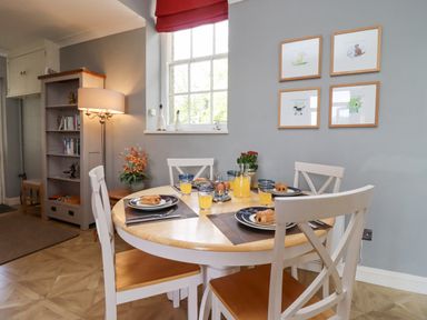 A dining area with a round table set with plates glasses orange juice and pastries four chairs a window bookshelf and framed pictures on the wall at The Tack Room in Lydney