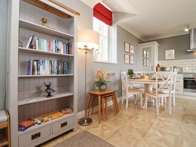 A kitchen and dining area with a bookshelf lamp and wooden tables with chairs at The Tack Room in Lydney