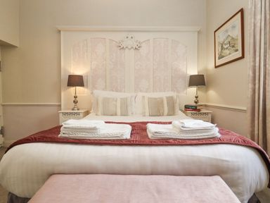 A bedroom with a bed with folded towels pillows bedside tables with lamps and a framed picture on the wall at The Tack Room in Lydney