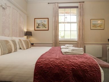 A bedroom with a bed covered in white sheets and a red blanket with folded towels on top at The Tack Room in Lydney