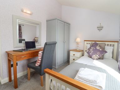 A bedroom with a single bed a wooden desk with a laptop a grey wardrobe and a bedside table at The Tack Room in Lydney