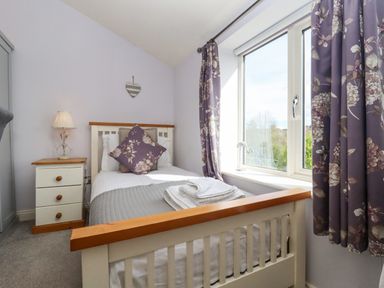 A bedroom with a single bed bedside table lamp and floral curtains at The Tack Room in Lydney