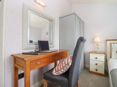 A bedroom with a wooden desk laptop and chair next to a wardrobe and bedside table with a lamp at The Tack Room in Lydney
