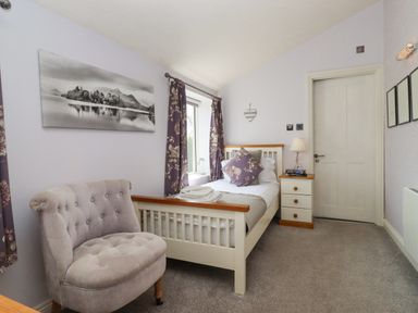 A bedroom with a single bed a chair a bedside table and a door at The Tack Room in Lydney