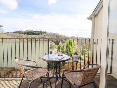 A small outdoor patio with two wicker chairs and a round glass table with champagne glasses and bottle at The Tack Room in Lydney