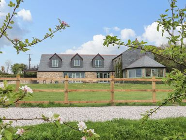 A stone house with a slate roof and wooden fence with green lawn and flowering tree branches at Higher Kernick View Helland near Blisland