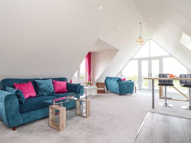 An attic living room with blue sofas pink cushions glass coffee table and a dining area with stools at Higher Kernick View in Helland near Blisland