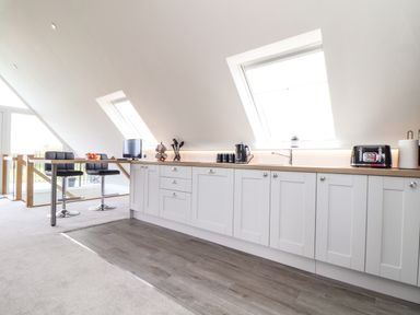 A kitchen with white cabinets a wooden countertop bar stools and windows on a sloped ceiling at Higher Kernick View in Helland near Blisland