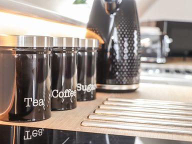 Black labeled containers for tea coffee and sugar on a countertop with a black kettle at Higher Kernick View in Helland near Blisland