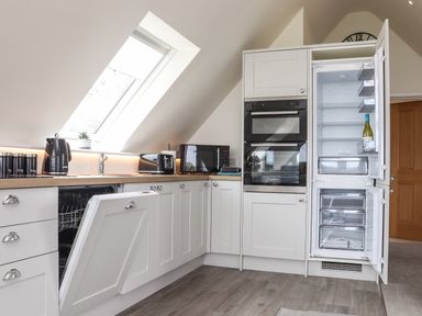 A kitchen with white cabinets an open dishwasher and fridge a microwave and toaster on the countertop at Higher Kernick View in Helland near Blisland