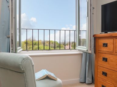 An open window with a view of trees a chair with an open book and a wooden dresser with a television Higher Kernick View Helland near Blisland