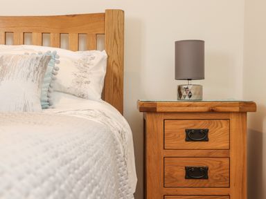 A wooden bed with white bedding and pillows next to a wooden bedside table with a lamp at Higher Kernick View in Helland near Blisland