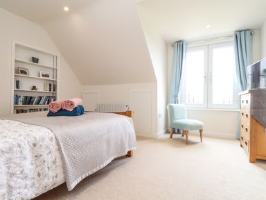 A bedroom with a bed and folded towels near a bookshelf a chair by the window and a wooden dresser at Higher Kernick View Helland near Blisland