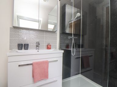 A bathroom with a white sink cabinet a pink towel on the handle two cups and a bottle on the sink and a glass shower enclosure at Higher Kernick View in Helland near Blisland