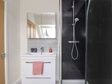 A bathroom with a white sink cabinet pink towel mirror and a black shower stall at Higher Kernick View in Helland near Blisland