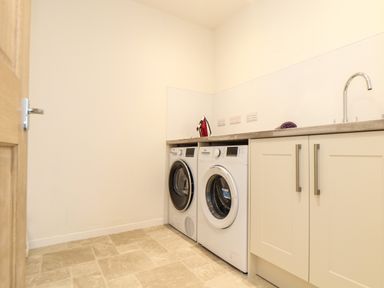 A utility room with a washing machine and dryer under a countertop with an iron and a sink at Higher Kernick View Helland near Blisland