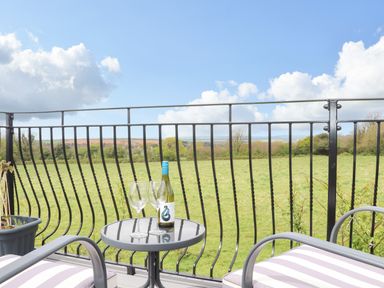 A balcony with two chairs a small round table with a bottle and two glasses overlooking a green field at Higher Kernick View in Helland near Blisland
