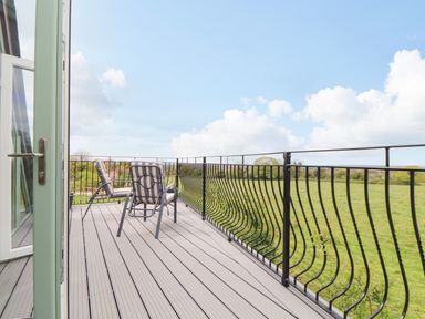 An outdoor balcony with two chairs and metal railing overlooking a grassy field at Higher Kernick View in Helland near Blisland