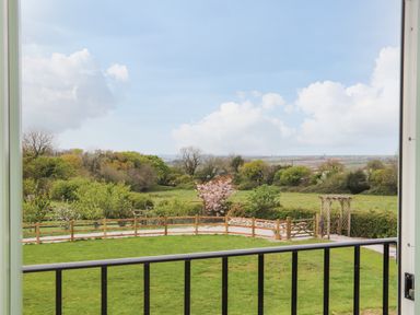 A view of a grassy garden with a wooden fence and a gate overlooking trees and countryside at Higher Kernick View in Helland near Blisland