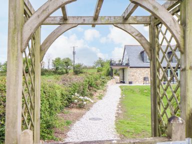 A gravel path leading to a stone house with a wooden archway and garden hedge at Higher Kernick View in Helland near Blisland