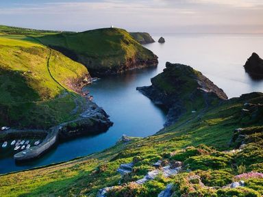 A coastal landscape with rocky cliffs green grass and small boats docked at a harbor at Higher Kernick View Helland near Blisland