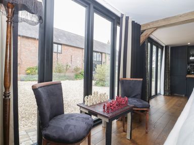 A small table with a chess set between two chairs near large glass doors in a room with wooden floors at The Courtyard - Hilltop Barn in Winterborne Zelston near Wareham