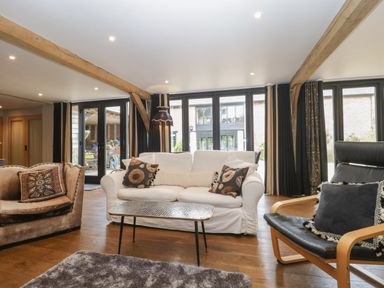 A living room with a white sofa, armchairs, a coffee table, wooden beams, and large windows at The Courtyard - Hilltop Barn in Winterborne Zelston near Wareham