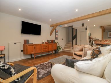 A living room with wooden cabinet and wall mounted TV at The Courtyard - Hilltop Barn Winterborne Zelston near Wareham
