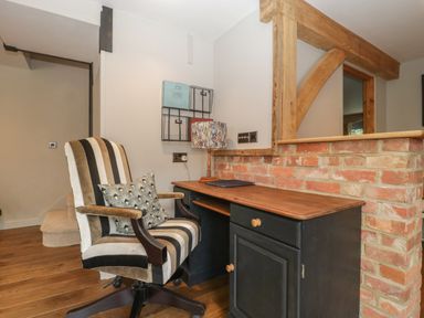A home office area with a striped office chair, wooden desk, table lamp, and brick half wall at The Courtyard - Hilltop Barn in Winterborne Zelston near Wareham